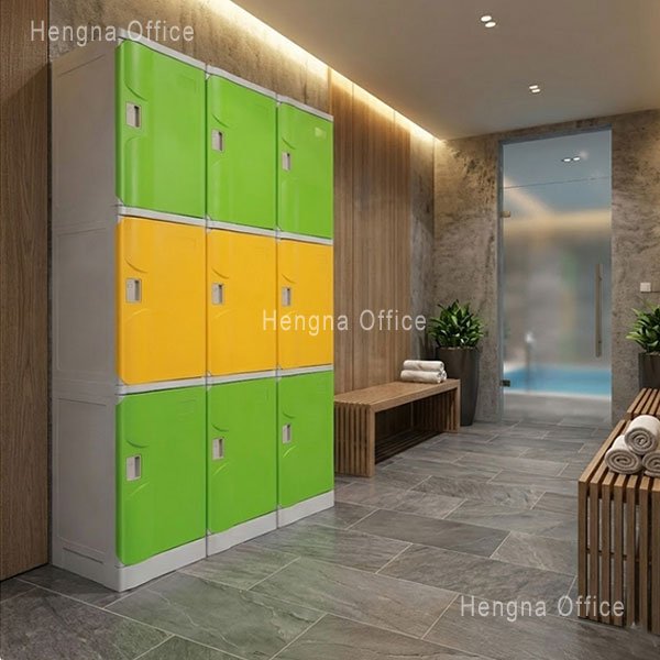 Front view of 9-door 3-tier ABS locker in green and yellow two-tone layout. Each compartment features individual cam lock handle, nameplate window, and ventilation slots. Clean gym or fitness center setting with wooden bench nearby.